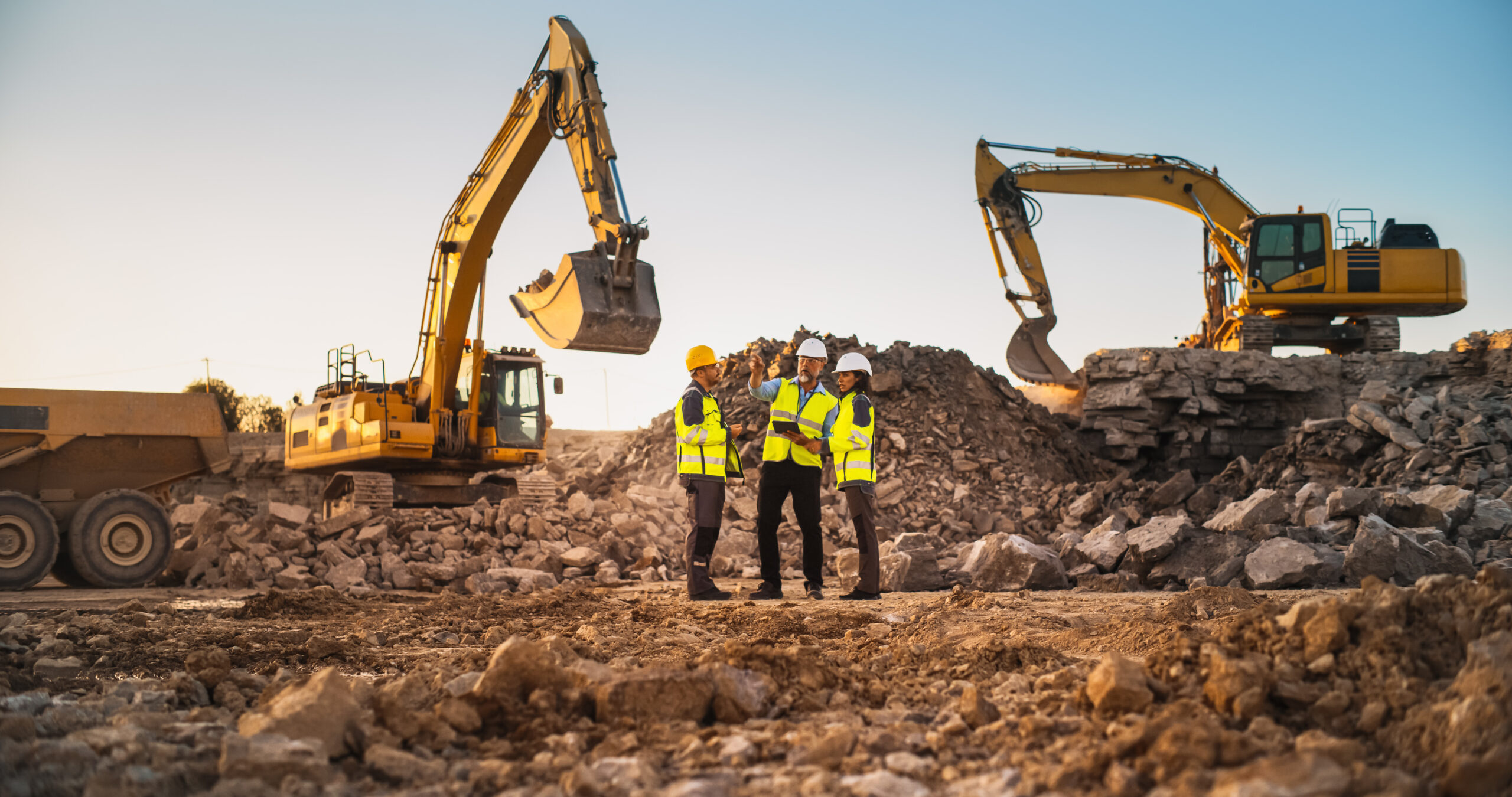 Construction Site With Excavators on Sunny Day: Diverse Team Of Male And Female Real Estate Developers Discussing Project. Engineer, Architect, Inspector Talking About Apartment Building, Using Tablet